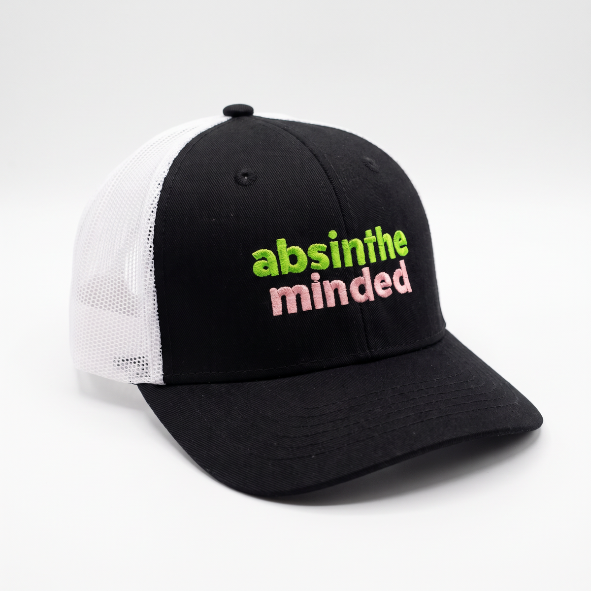 A black and white trucker hat with the embroidered text 'absinthe minded' in lime green and pink on the front panel, set against a clean white background.